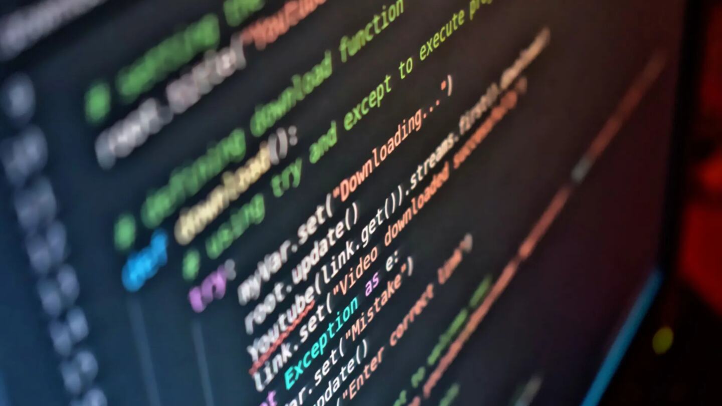Developer reviewing software code on a monitor beside a smartphone